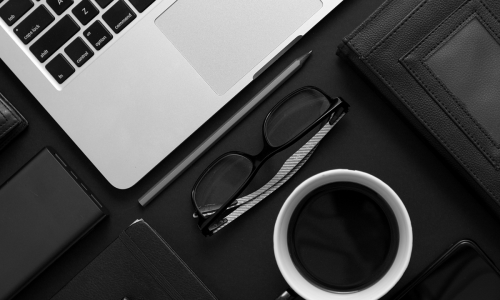 Desk with laptop, glasses, coffee, pen, notebook